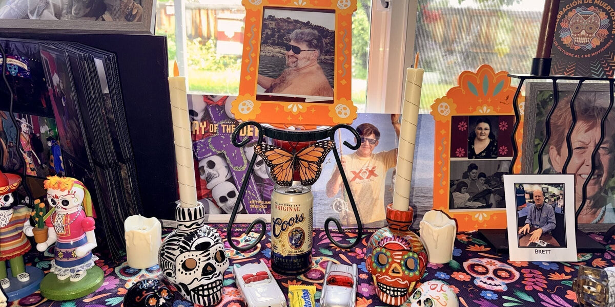 A home ofrenda for Día de Muertos honoring Carrie's father, with his photograph in an orange frame, a Coors can, toy Corvettes, a Butterfinger, candles, and sugar skulls