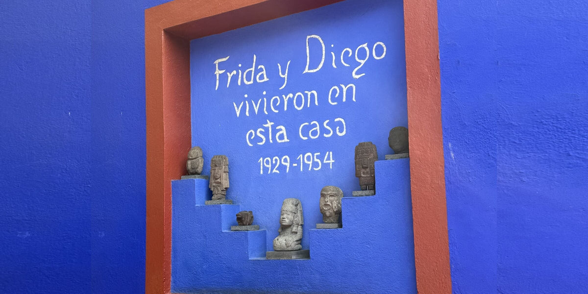 A cobalt blue wall at Casa Azul in Coyoacán with the inscription Frida y Diego vivieron en esta casa 1929-1954 and a row of pre-Hispanic stone figures