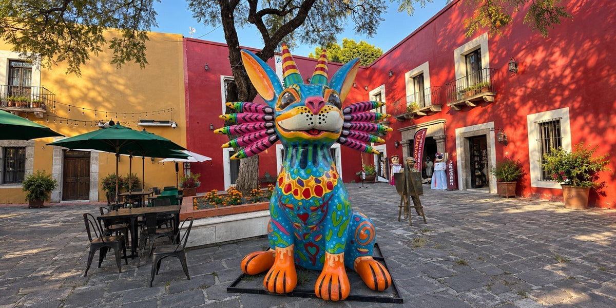 A giant blue alebrije with striped horns, rabbit ears, and pink spines in a courtyard of red colonial buildings in the Barrio del Artista, Puebla, Mexico